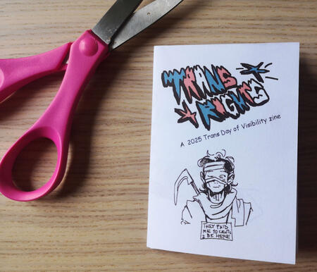 Photograph of a folded zine titled Trans Rights: a 2025 Trans Day of Visibility zine. Under the title there is a portrait of a man, drawn by opt1gan, with a sign around his neck that says "they paid me 10 cents to be here".